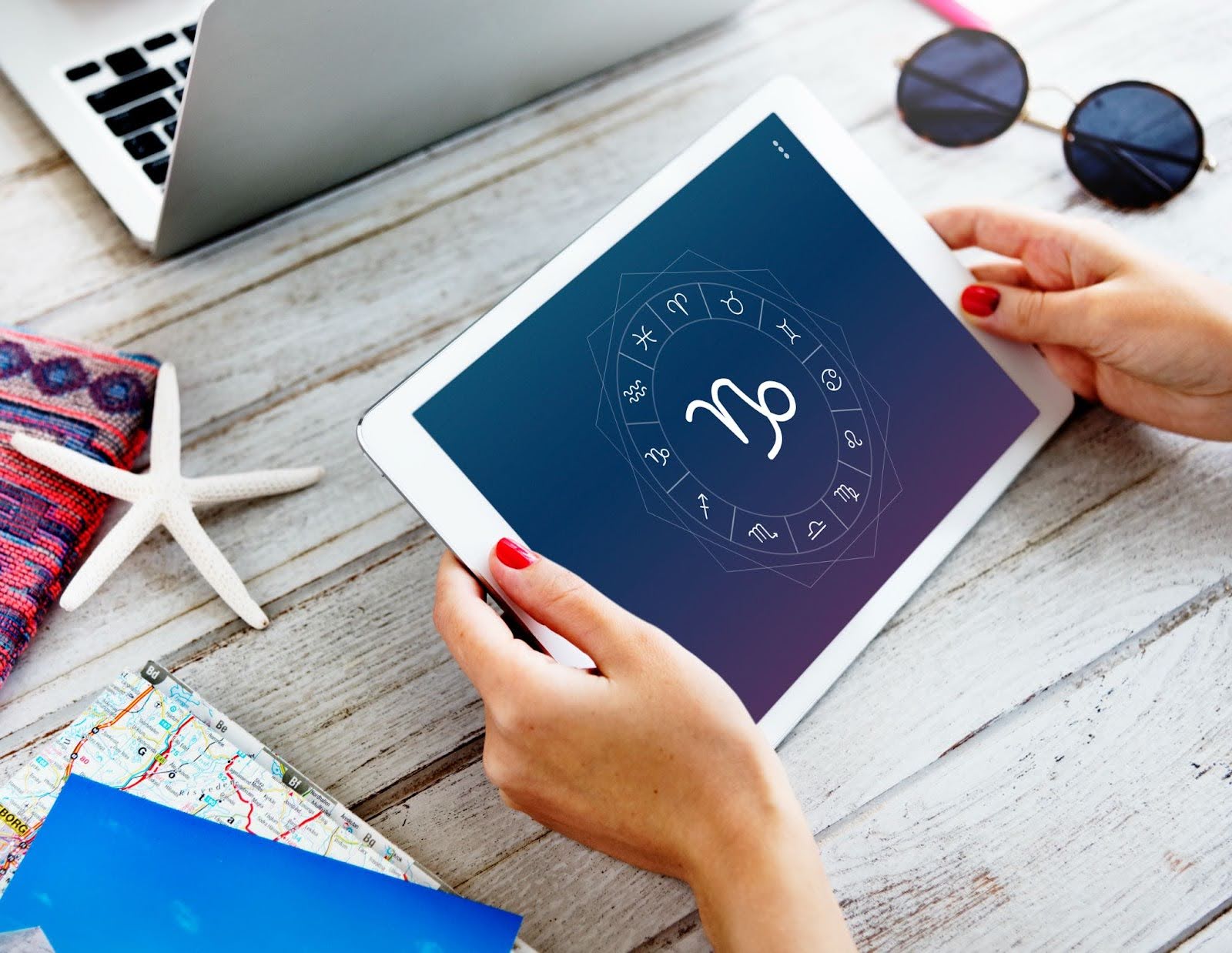 Person holding a tablet displaying a zodiac chart on a work desk with notebooks and accessories, symbolising the sixth house focus on daily routines and disciplined effort in Vedic astrology.